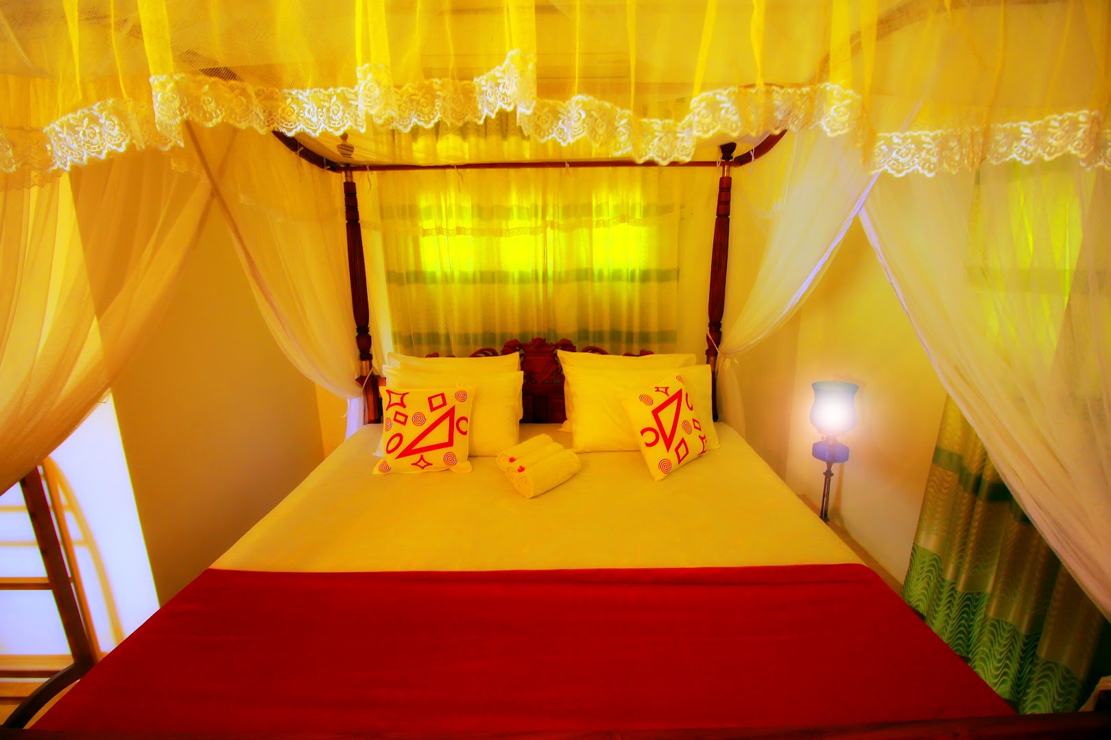 Guest bed with white mosquito netting and red bed cover