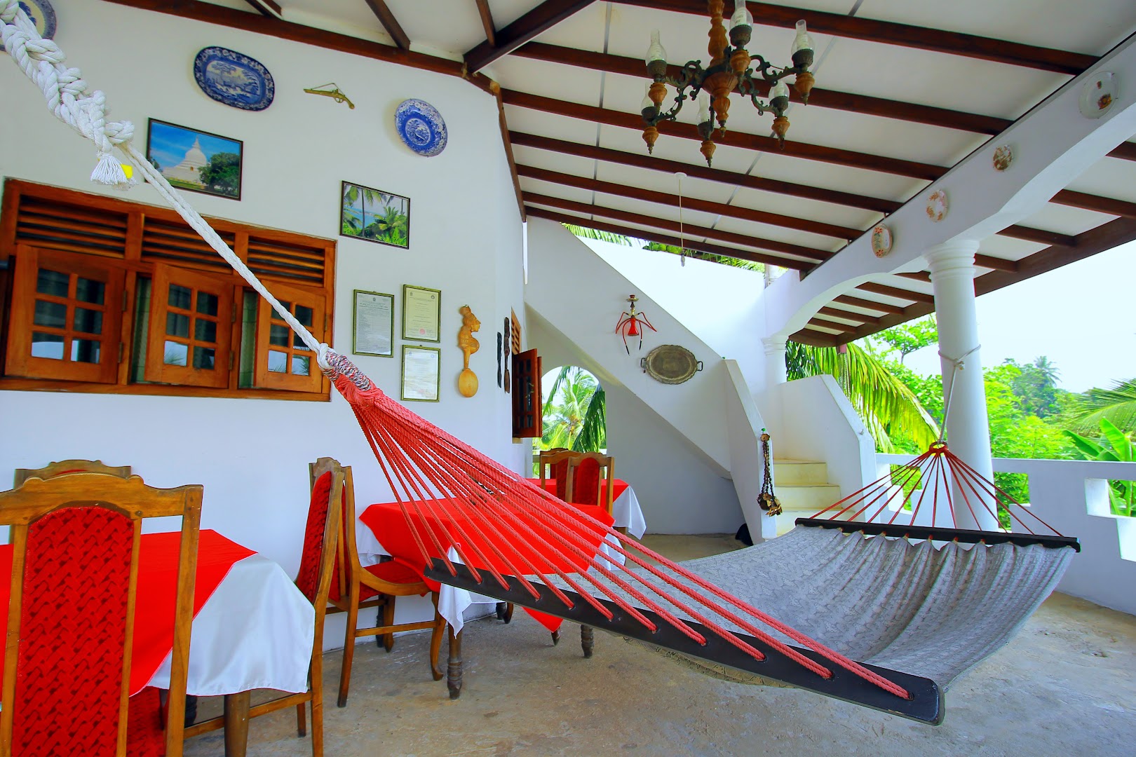 Open villa veranda with hammocks, dining tables, white arches, and garden views