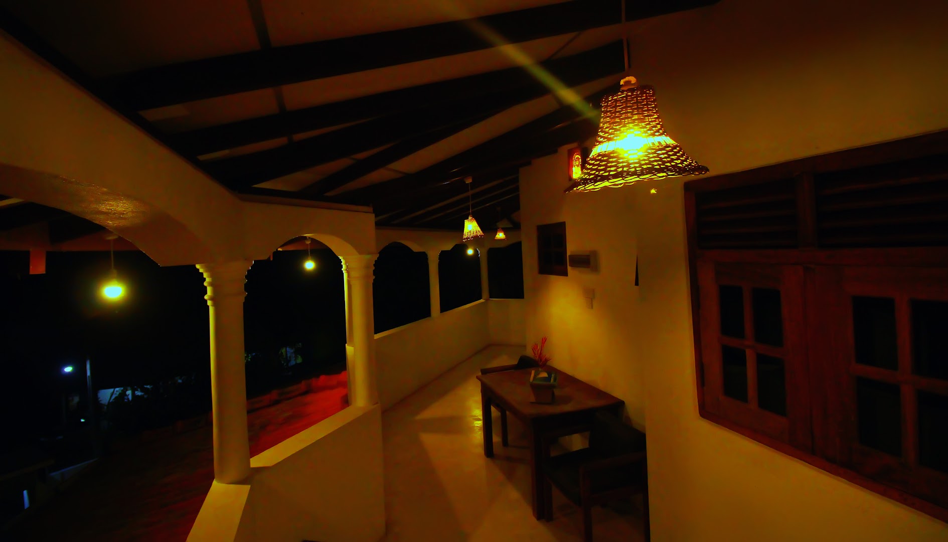 Villa veranda at night with woven pendant lights and white arches
